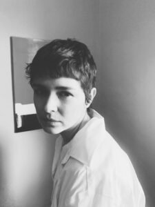 A black and white photograph of a woman in three-quarter turn, looking at the camera. She has short hair and is wearing a white dress shirt.