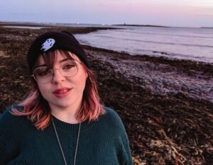 A white woman with wavy brown hair and blue eyes smiles at the camera.