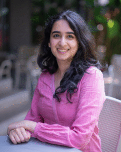 Photo of a smiling brown woman sitting down with long black hair, wearing a long-sleeved pink top.