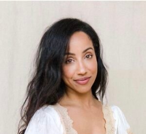 Photo of the author, Adrienne Thurman, who has brown skin, brown eyes, and long straightened black hair. She is smiling with closed lips, seated against a soft neutral background, wearing a white blouse with nude colored lace trim.