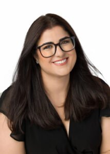 Alexis Calder, a white woman with medium length dark hair and glasses. She has her head tilted slightly and is smiling. The photo shows from shoulders up.