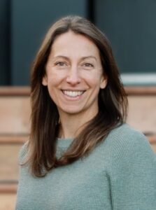 Smiling woman with mid-length brown hair in a green sweater.