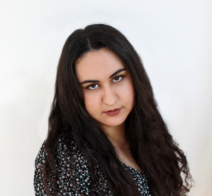 Amanda Rizkalla, a woman with long wavy brown hair, looks at the viewer with her head slightly tilted.