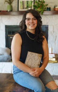 Anna Mercier, the author, sits on a table clutching a bound copy her husband made of her first book. She has got a huge grin and ripped jeans because that's who she truly is.