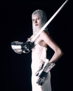 Ava Lauren Grayson, a female author in knight's chainmail, white dress, and holding a sword.