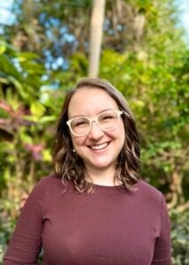 Brianna Jett, a white woman with should length brown curly hair and white glasses.