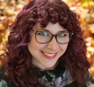 Carrie Lee South, a white woman with dark, curly hair, smiling against a background of fall leaves.