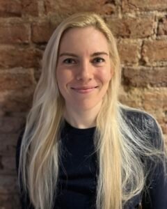 Connie Kitson, a white woman with long, light blonde hair, standing in front of an exposed-brick wall. Only her head and shoulders are visible in the photo.