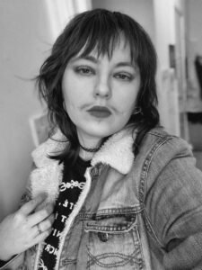 Dorian, who is white with a dark wolf-cut hairstyle and a thin moustache, faces the viewer relatively close up with a neutral expression. It is set against a plain background of a living room door.