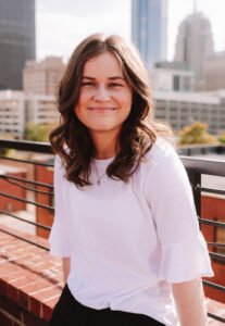 A photo of Emma Jackson in a white shirt with a city landscape in the background.