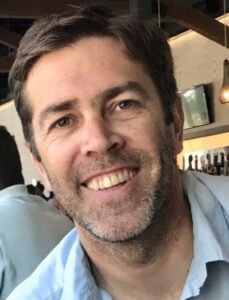 Eric Scot Tryon, a middle-aged white man, with short brown hair, wearing a light blue collared shit. He is looking at the viewer with a smile.