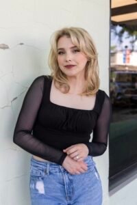 Grace Morrow, a white woman smiling at the camera with blonde hair wearing a black shirt and jeans.