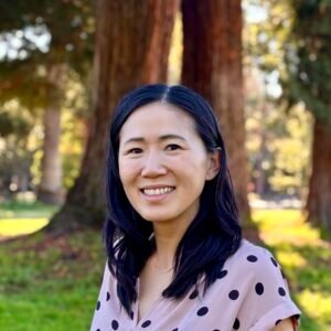 Jasmine Fang, an Asian female with dark hair and a pink shirt is outside with a smile. She is outdoors.