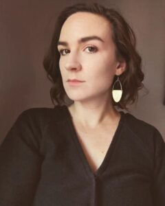 Author Julia Laurel, a white woman with shoulder-length brown hair, a serious expression and gold geometric earrings.