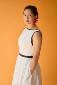 A half-Asian, half-white woman in a white dress against an orange background