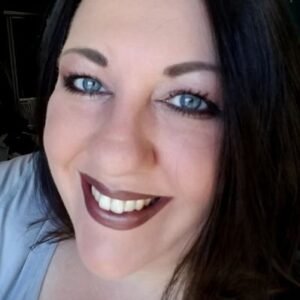 Maria Tureaud, a pale white Irish woman with long, black/brown hair and sapphire eyes smiles at the camera for a head shot.