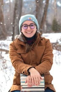 Molly Haniszewski sits with a stack of books on their lap.