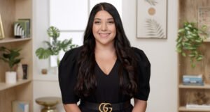 Nidhi Tewari, MSW, LCSW, a brown woman with long black hair, sits in an office with plants in the background. She is looking at the viewer and smiling.