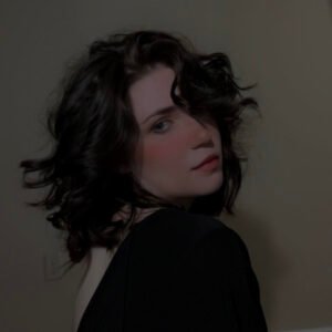 R. A. Betzer, or Rory, a white woman with short, curly, dark hair looking over her shoulder with a slight smile.