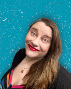 Rosie J. Potter, a white woman with long light brown hair, is looking at the camera with a slight smile. She is wearing bright red lipstick, a rainbow shirt, and a necklace in this headshot style photo.