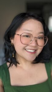 A girl smiles at the camera, dressed in a green dress with a square neck.