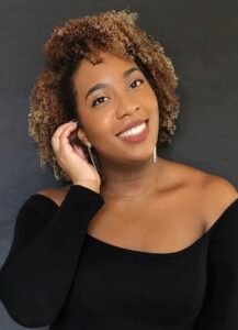 Shari B. Pennant, a smiling Black woman with blonde curly hair, in a black shirt against a gray background.