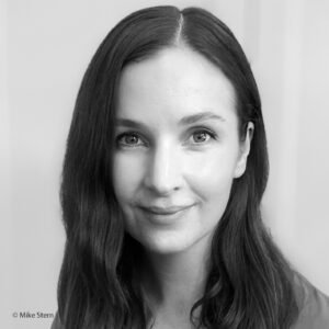 Sophie Stern, a white woman with medium length dark hair, in front of a white background. She is looking at the viewer with a slight smile. The photo is in black and white.