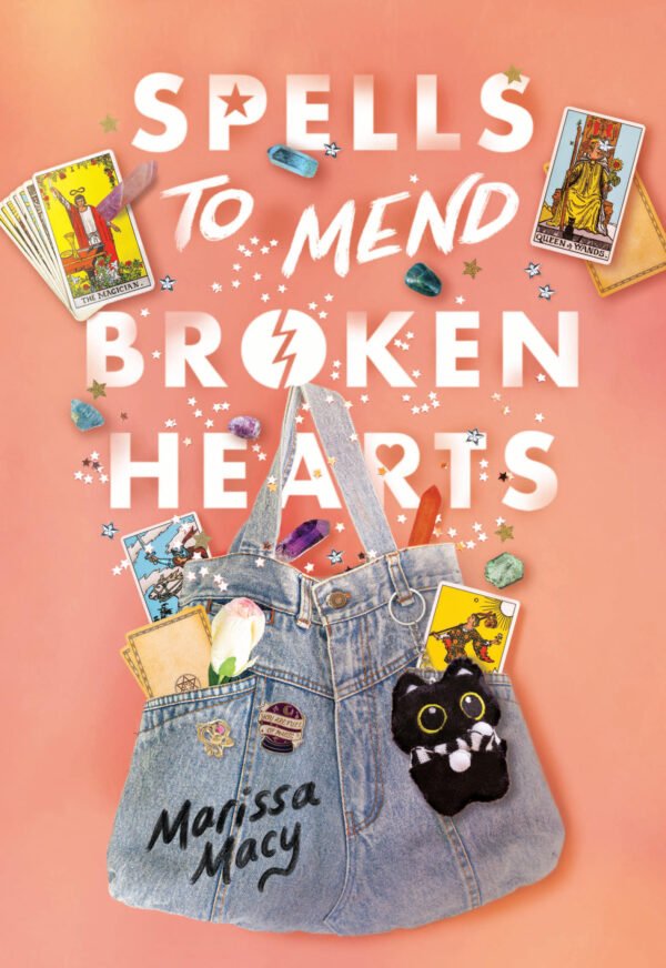 Cover of Spells to Mend Broken Hearts by Marissa Macy. The design shows a pink-orange background with sparkles, tarot cards, crystals, and a denim tote bag with tarot cards coming out of it. The bag has charms and a black cat keychain.